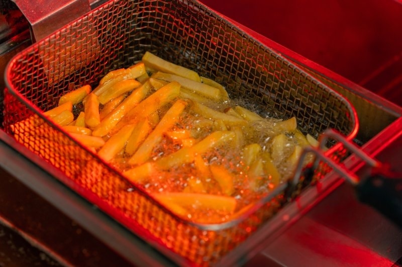 Basket of French fries cooking in bubbling hot oil inside a deep fryer.