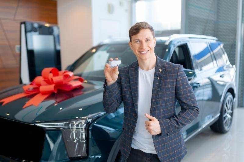 Male adult in suit buying new suv at car dealership with red ribbon gift.