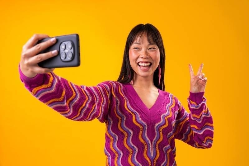 Young woman smiling while taking a selfie and making a peace sign.