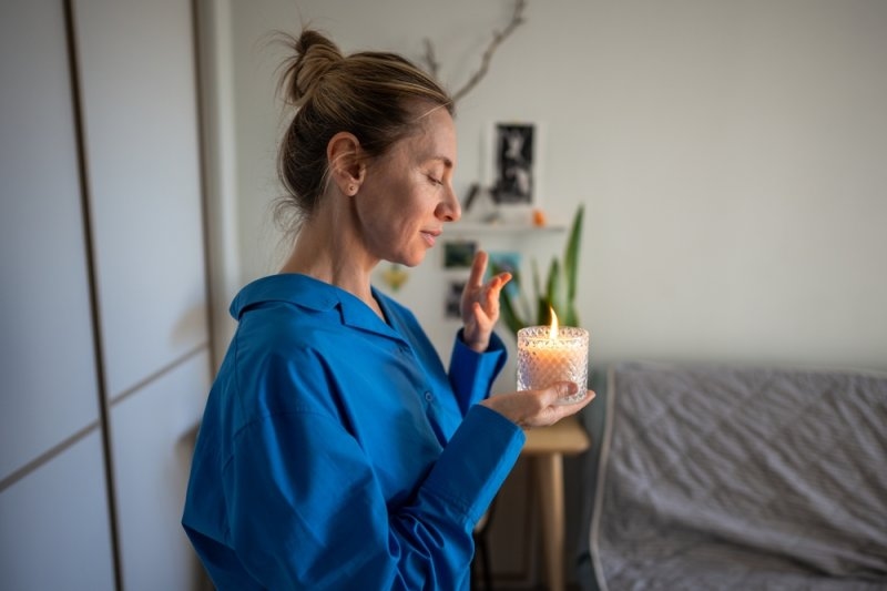 Calm middle-aged woman enjoy smelling lighted scented aromatic candle.