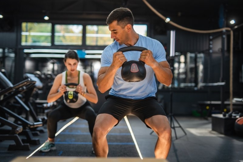 Personal coach do kettle bell squat exercise with client at gym