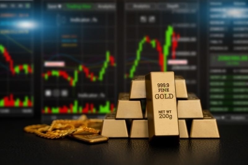 Fine gold bars displayed in front of stock market charts.