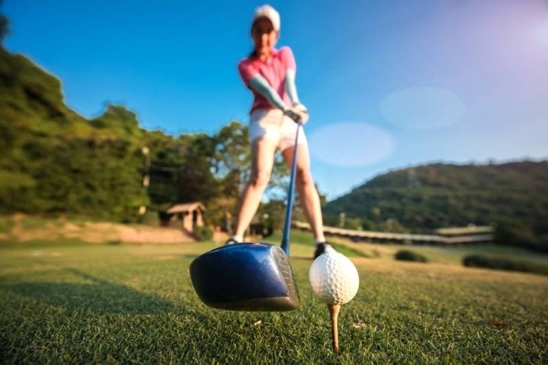 Golfer lining up a drive with a driver behind a golf ball on a tee.