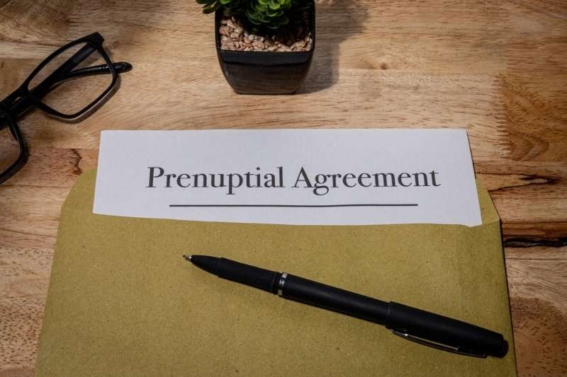 Prenuptial agreement document on a desk with a pen, glasses, and small plant nearby.