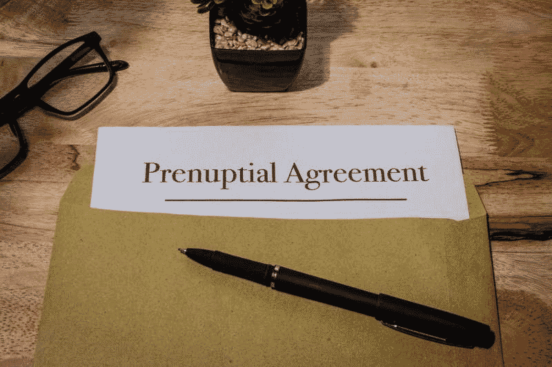 Prenuptial agreement document on a desk with a pen, glasses, and small plant nearby.
