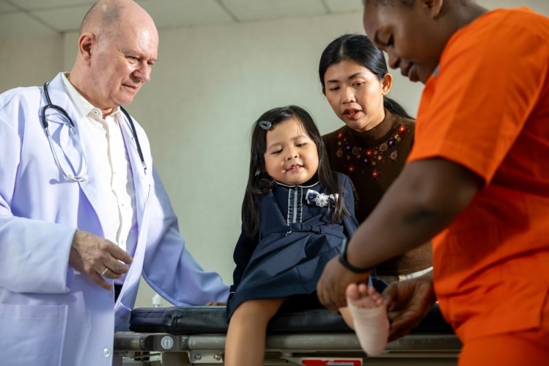 Little asian girl having accident with ankle sprain gets treatment from nurse and senior doctor in the hospital.