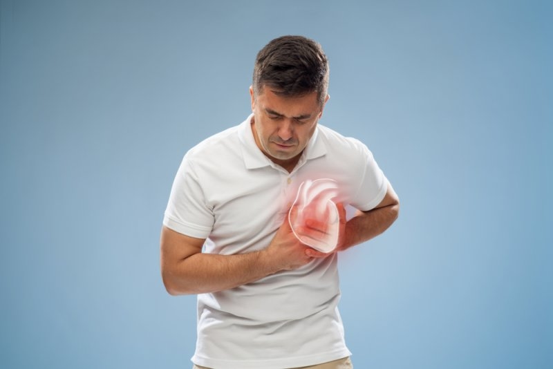 Man experiencing chest pain while holding his chest, with a glowing anatomical heart illustration highlighting the affected area.