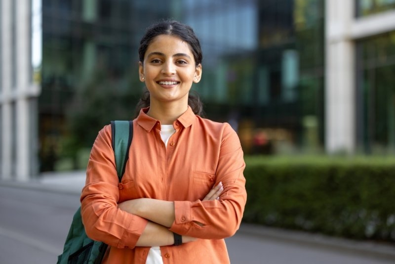 A smiling student with a backpack standing outside a school or educational building.