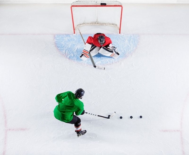 Top-down view of a hockey player practicing shots against a goalie on the ice.