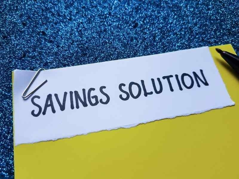 Close-up of a handwritten note reading “SAVINGS SOLUTION” placed on a yellow surface with a pen and paper clip.