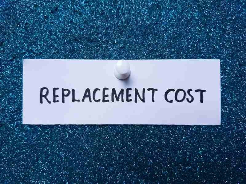 A white note displaying the words “REPLACEMENT COST” pinned against a dark blue textured background.