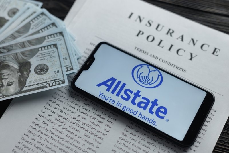 Smartphone displaying the Allstate logo placed on an insurance policy document beside U.S. dollar bills.