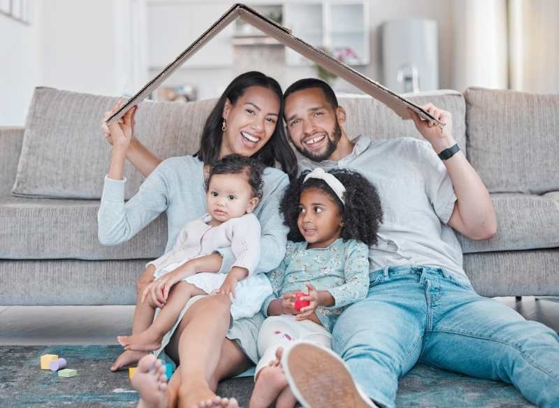 A smiling family sitting on a couch beneath a house-shaped frame.