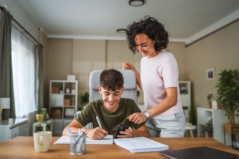 Mother helping her son with homework at a desk in a bright home setting.