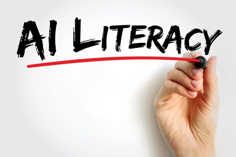 “AI LITERACY” are written in bold black lettering on a white background, with a hand using a marker to underline the phrase in red.