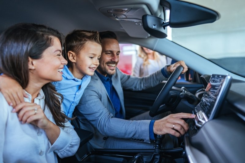 A smiling family sits together inside a vehicle, with the driver interacting with the infotainment system.