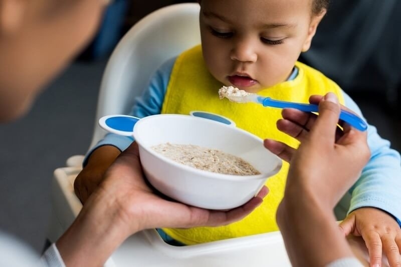 mother feeding little baby with porridge at home