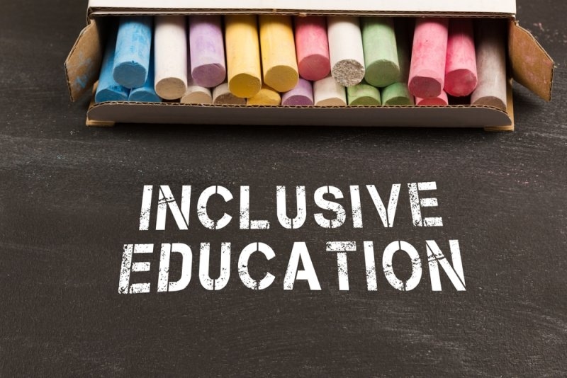 Box of colorful chalk above the words “INCLUSIVE EDUCATION” on a blackboard.