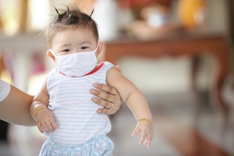 A baby wearing a protective face mask and being supported by an adult.