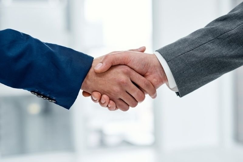 A close-up of two professionals in business suits shaking hands in a bright, modern office.