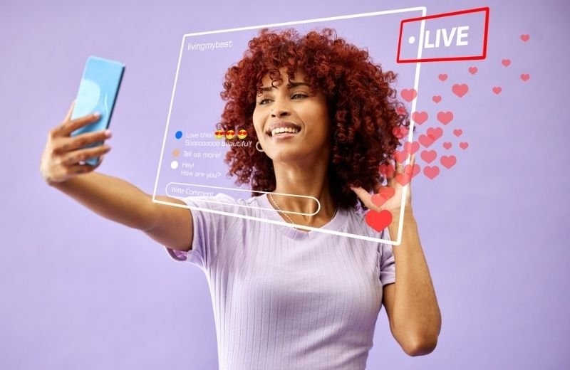 A woman holds a smartphone while appearing on a simulated social media livestream interface, with comments and floating heart icons.