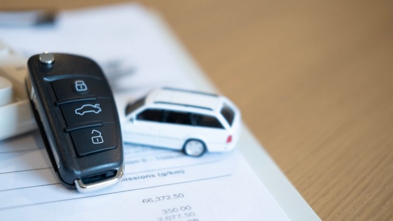car keys and a miniature car on top of car insurance papers