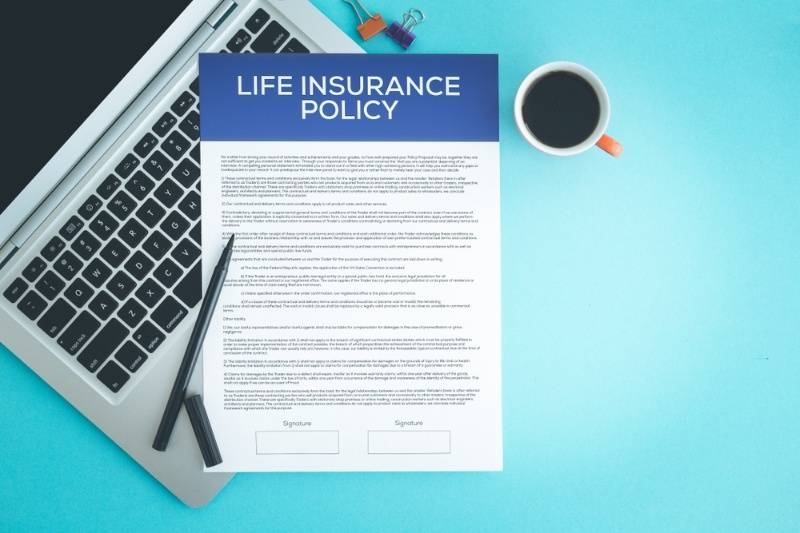 Life insurance policy document placed on a desk with a laptop, coffee cup, and pen, representing financial planning and coverage.