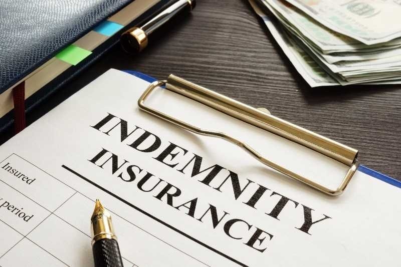 Indemnity insurance document on a clipboard with a fountain pen and cash on a desk.