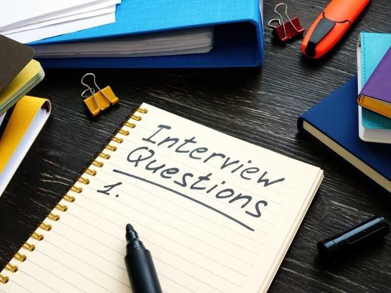 Notebook labeled "Interview Questions" with a pen, binders, and office supplies on a desk.