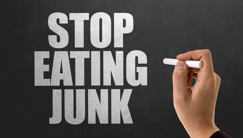 Hand writing “STOP EATING JUNK” in large white letters on a black chalkboard.