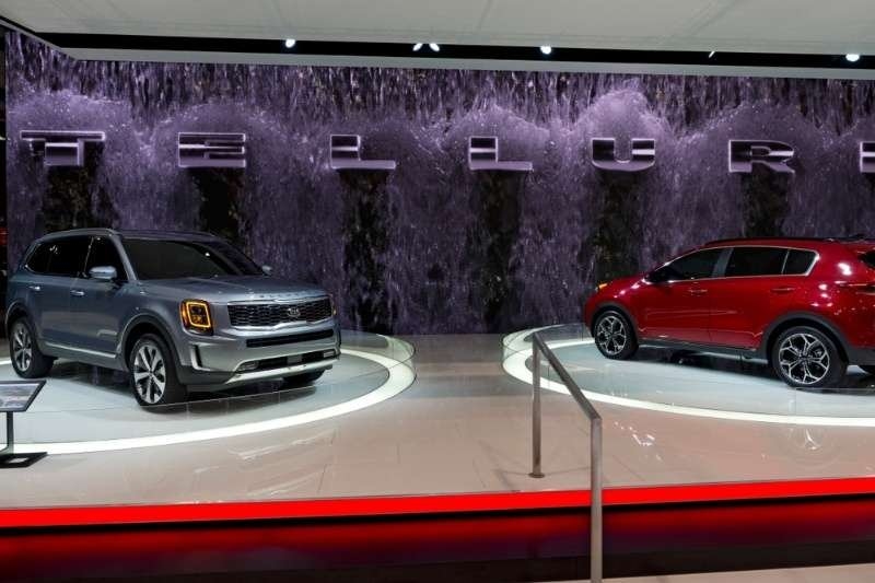 Two Kia Telluride SUVs displayed on illuminated platforms at an automotive exhibition with branded backdrop and showroom lighting.