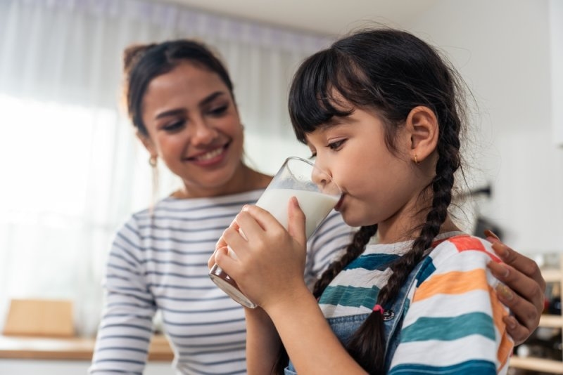 ittle kid holding a cup of milk and drinking with mother.