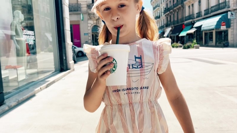 A little girl drinks a cold beverage from Starbucks while walking on the street