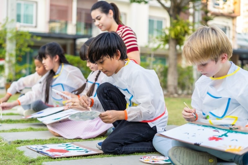 Group of student coloring on painting board outdoors in school garden.
