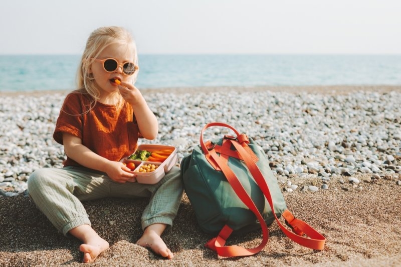 Child girl with lunchbox eating vegetables outdoor during travel vacation