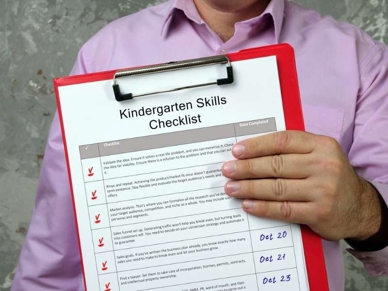 Person holding a clipboard with a kindergarten skills checklist.