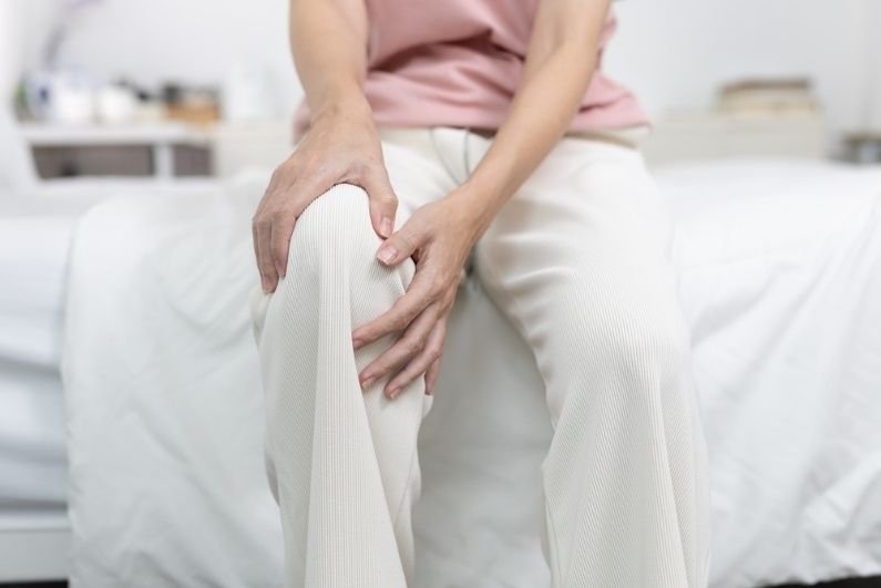 2. Person seated on a bed holding a painful knee, illustrating knee discomfort, injury, or joint pain.