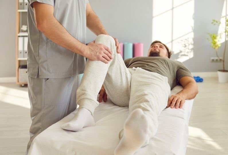 1. Physical therapist assisting a patient with a leg mobility exercise on a treatment table during a rehabilitation session.