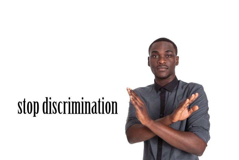 Man crossing his arms in an X gesture beside the words “stop discrimination” on a white background.