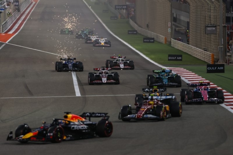 Formula 1 cars racing down a circuit during a Grand Prix, with multiple cars competing on the track.