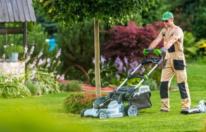 Landscaper operating a lawn mower while maintaining a residential garden with neatly trimmed grass and landscaped plants.