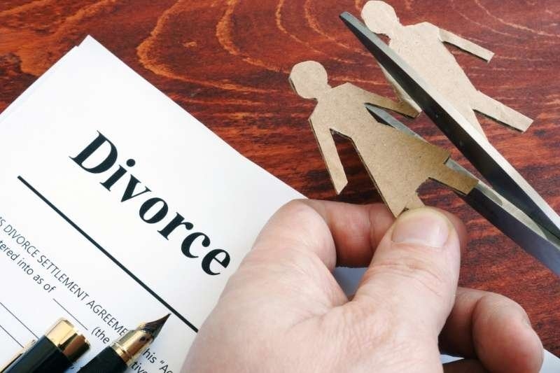 A hand holds a paper labeled “Divorce” alongside paper figures being separated with scissors.