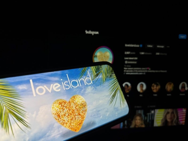 Smartphone displaying a Love Island USA screen with a heart-shaped image, set against a dark social media interface.