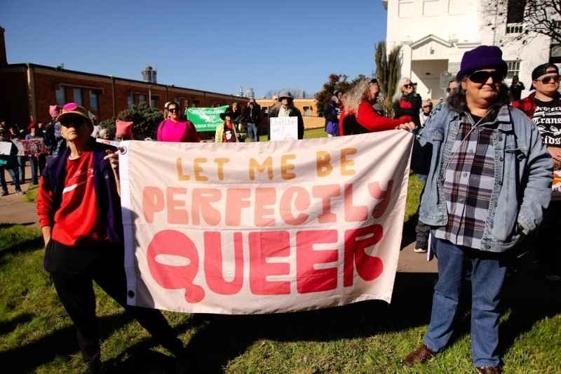 Participants at a public pride rally hold a banner reading "Let Me Be Perfectly Queer" during an LGBTQ+ rights demonstration.