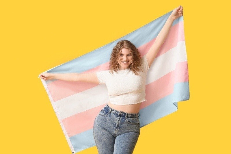 Beautiful young woman with transgender flag on yellow background.
