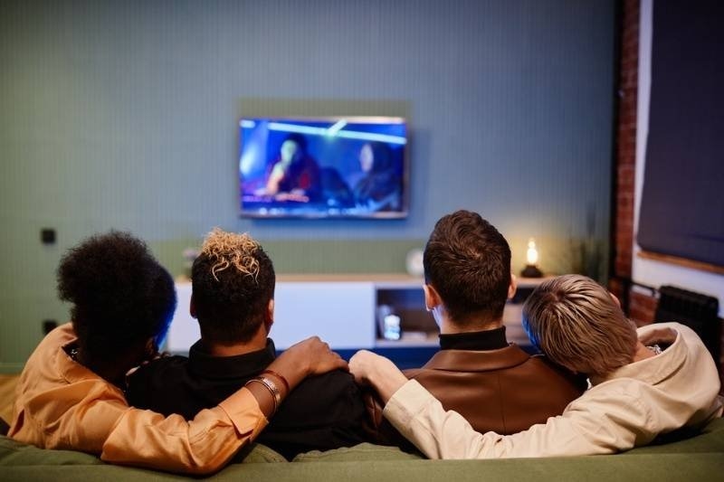 Group of friends relaxing on a couch while watching a movie on television.