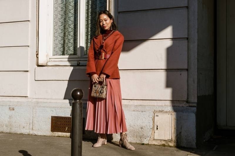 Fashionable woman wearing a coordinated jacket and pleated skirt while posing outdoors.