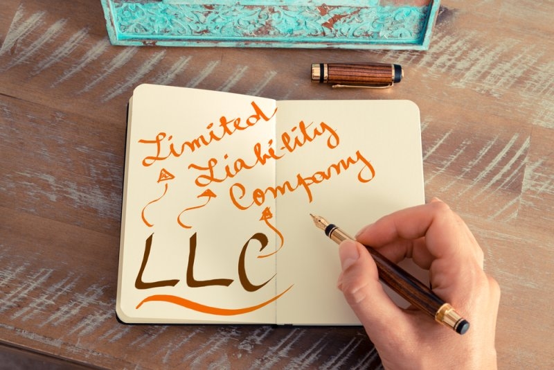 Person writing “Limited Liability Company” and “LLC” in a notebook with a fountain pen.