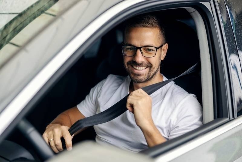 Smiling man with glasses actively fastening his seatbelt inside a modern vehicle