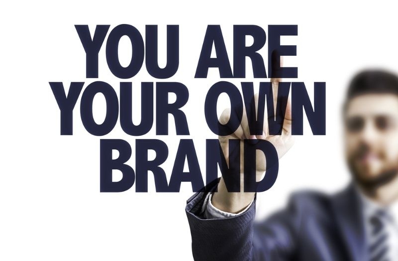 Businessman standing behind large text that says ‘You Are Your Own Brand.’